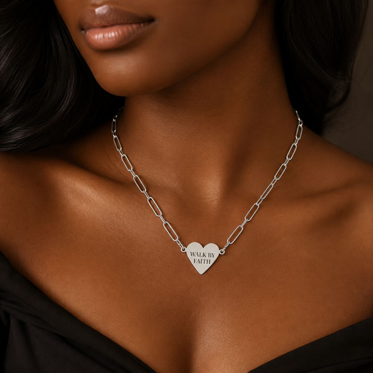 A close-up of a model wearing a silver paperclip chain necklace with a heart-shaped pendant engraved with the words 'WALK BY FAITH'.